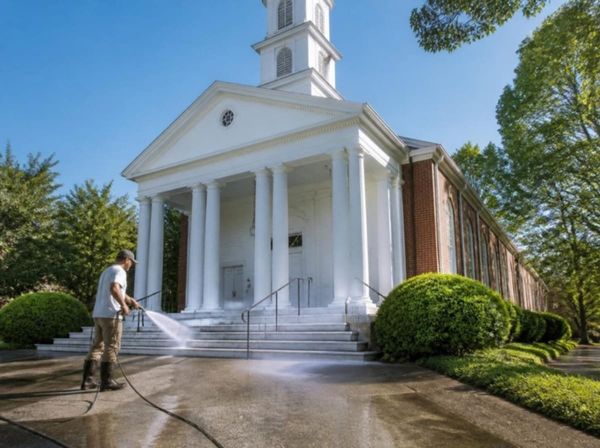 Technician soft washing the facade of a brick church